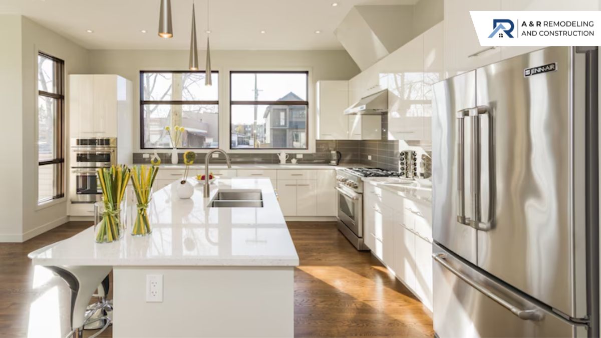 A bright, modern kitchen featuring white cabinets, stainless steel appliances, a large island with a sink, and pendant lights.
