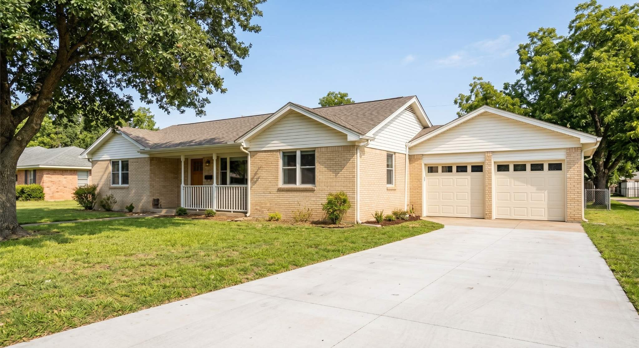 Completed garage addition on a beige brick home, featuring two new cream-colored garage doors and a newly poured concrete driveway replacing the grass.